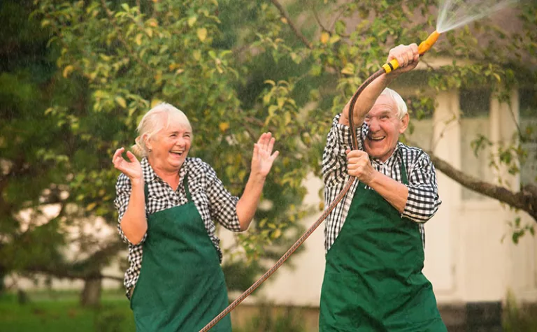 elderly couple playing with garden hose