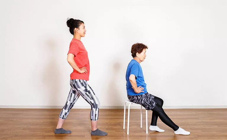 elderly woman doing chair yoga with trainer